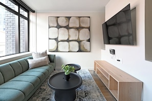 A modern living room with a sectional sofa, a coffee table, a TV mounted on the wall, and a large abstract painting. - Trendy Studio Apartment at The Tokyo in Central Cape Town City (Cape Town)