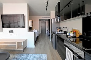 Una cocina moderna con horno integrado, un comedor con mesa de madera y una sala de estar con televisor grande.