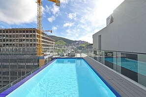 Una piscina en la azotea con vistas a una obra en construcción y una colina al fondo.