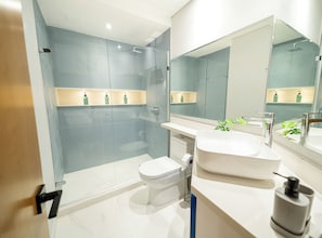 Un bany modern amb plat de dutxa de vidre, un lavabo blanc i un mirall gran.