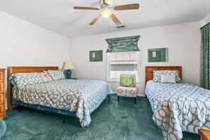 A bedroom with two beds, a ceiling fan, a window with curtains, and a small chair. - Shelley by the Seas  Beach Escape in N. Myrtle Beach, 3-bedroom house (North Myrtle Beach)