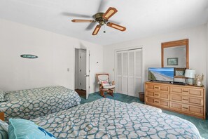 Une chambre avec deux lits, un ventilateur de plafond, une chaise, une commode et un téléviseur.
