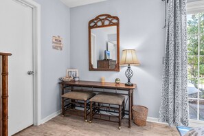 Une pièce comprenant une console en bois, deux fauteuils rembourrés, un miroir, une lampe et un panier en osier.