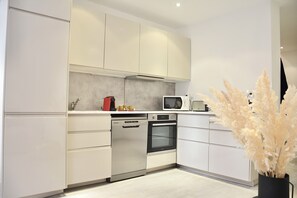 A modern kitchen with white cabinets, a dishwasher, an oven, a microwave, and a decorative plant. - M17—Elegant Duplex in Majorelle—Pool, Balcony, and Parking (Marrakech)