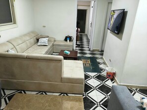A living room with a beige sofa, a coffee table, and a patterned rug. There is a television mounted on the wall and a door leading to another room. - Sea veiw BAHARI (Alexandria Governorate)