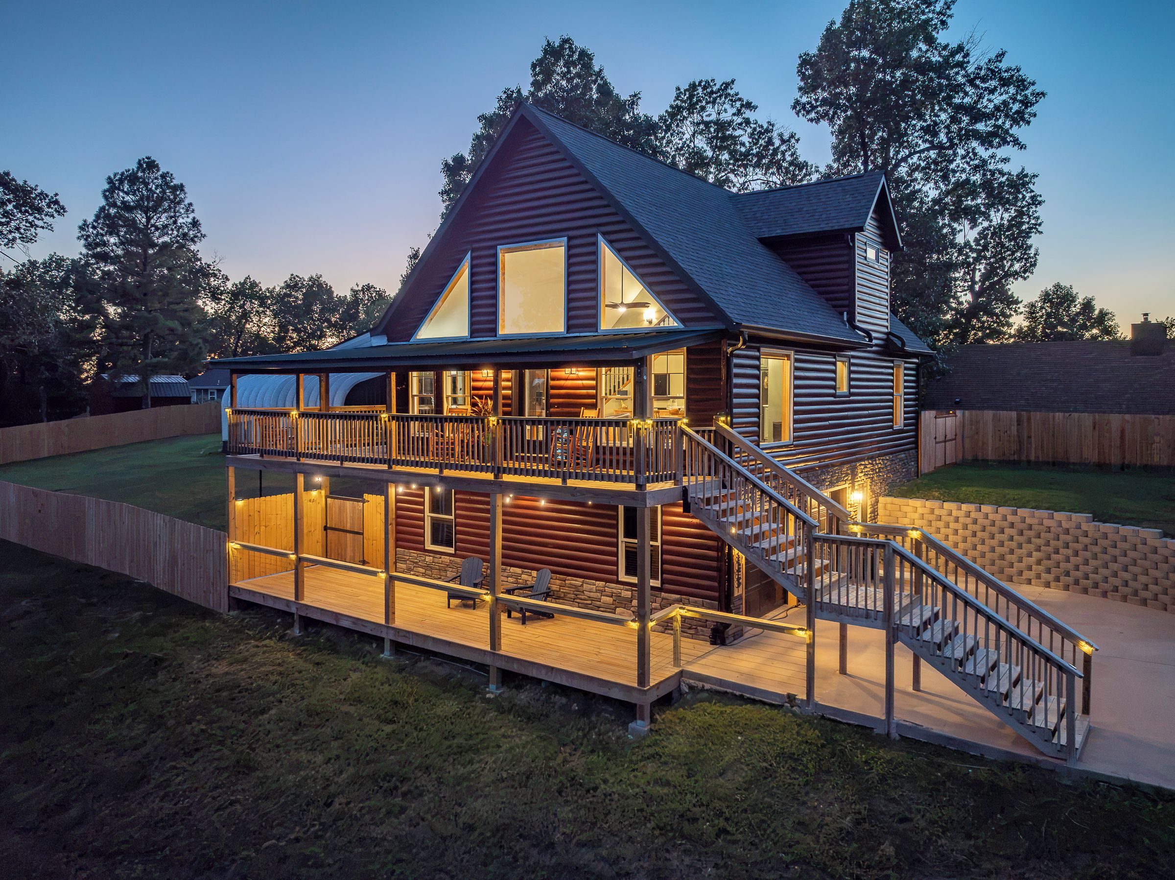Una cabaña de troncos con terraza, iluminación exterior y una escalera que conduce a la entrada principal.
