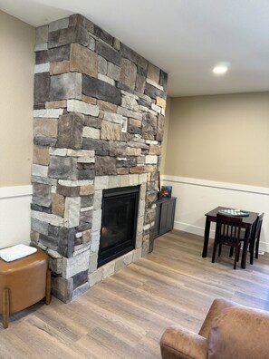 A living room with a stone fireplace, a wooden dining table with chairs, and a leather ottoman. - Luxury Montana Cabin on Rocky Mountain Front-Entrance to Bob Marshall Wilderness (choteau)
