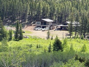 A modern two-story cabin with a covered porch, surrounded by dense forest. - Luxury Montana Cabin on Rocky Mountain Front-Entrance to Bob Marshall Wilderness (choteau)