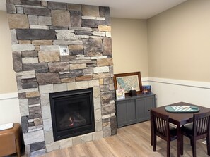 A stone fireplace with a modern design, a framed picture above it, and a table with chairs in front. - Luxury Montana Cabin on Rocky Mountain Front-Entrance to Bob Marshall Wilderness (choteau)