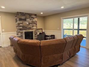 A living room with a stone fireplace, a brown sectional sofa, and a dining area with a table and chairs. - Luxury Montana Cabin on Rocky Mountain Front-Entrance to Bob Marshall Wilderness (choteau)