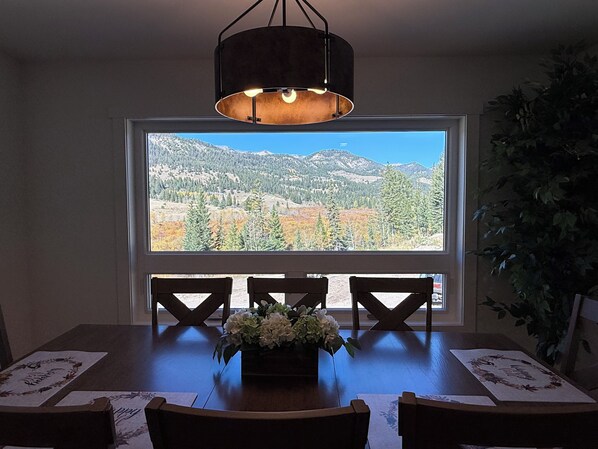 A dining area with a table and chairs, a window with a view of mountains, and a hanging light fixture.