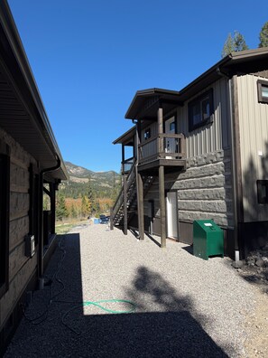 A wooden cabin with a balcony, a gravel driveway, and a mountain backdrop. - Luxury Montana Cabin on Rocky Mountain Front-Entrance to Bob Marshall Wilderness (choteau)