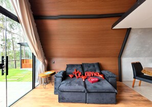 A modern living room with a sofa, a small table, and a view of the outdoors. - Chalet 4 Elements - Privacy and a breathtaking view 15 minutes from the city center. (Vale do Paquequer)