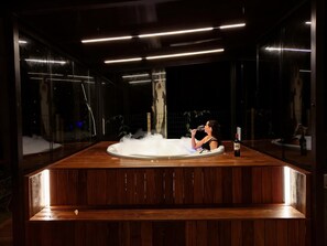 Una persona relajándose en un jacuzzi con una botella de vino al lado.