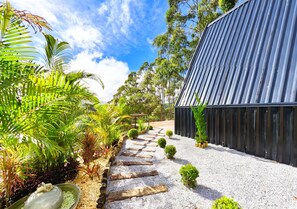 A pathway leading to a modern building with a corrugated metal roof, surrounded by lush greenery and a clear sky. - Chalet 4 Elements - Privacy and a breathtaking view 15 minutes from the city center. (Vale do Paquequer)