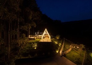 Una casa moderna con techo triangular, rodeada por un jardín cuidado y un camino que lleva a la entrada.