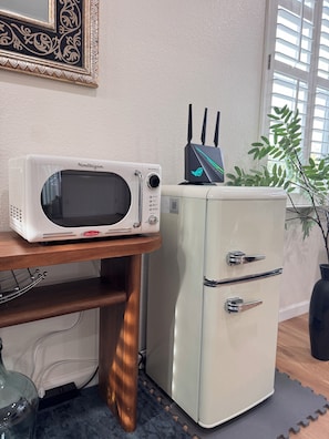 A retro-style refrigerator with a built-in microwave on top, a power strip, and a potted plant beside it.