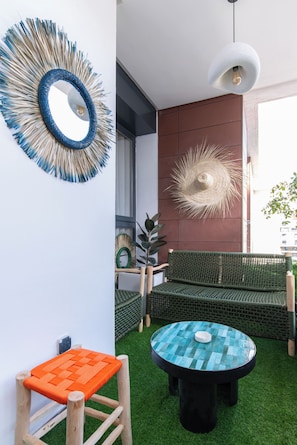 A modern outdoor seating area with a green sofa, a small orange table, and a round table with a blue mosaic top. - Family Canopy · Bright 3-bedroom apartment, 2 balconies, garage – Casablanca (Casablanca)