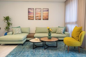 Una sala moderna con un sofá verde, un sillón amarillo y una mesa de centro. Hay tres cuadros enmarcados en la pared y una planta en maceta.