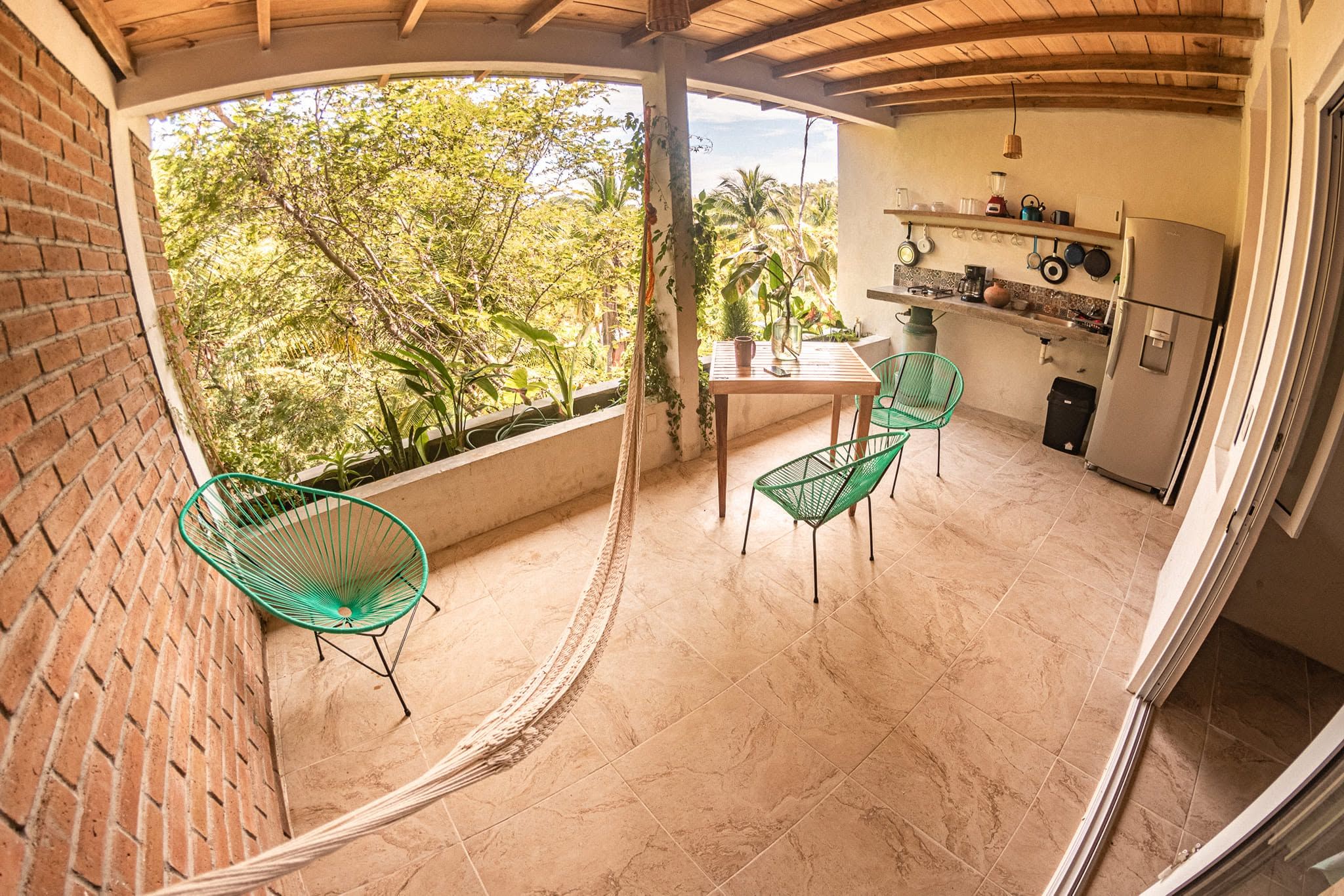 Una cocina con techo de madera, una zona de comedor con sillas verdes y vistas a árboles a través de una ventana.