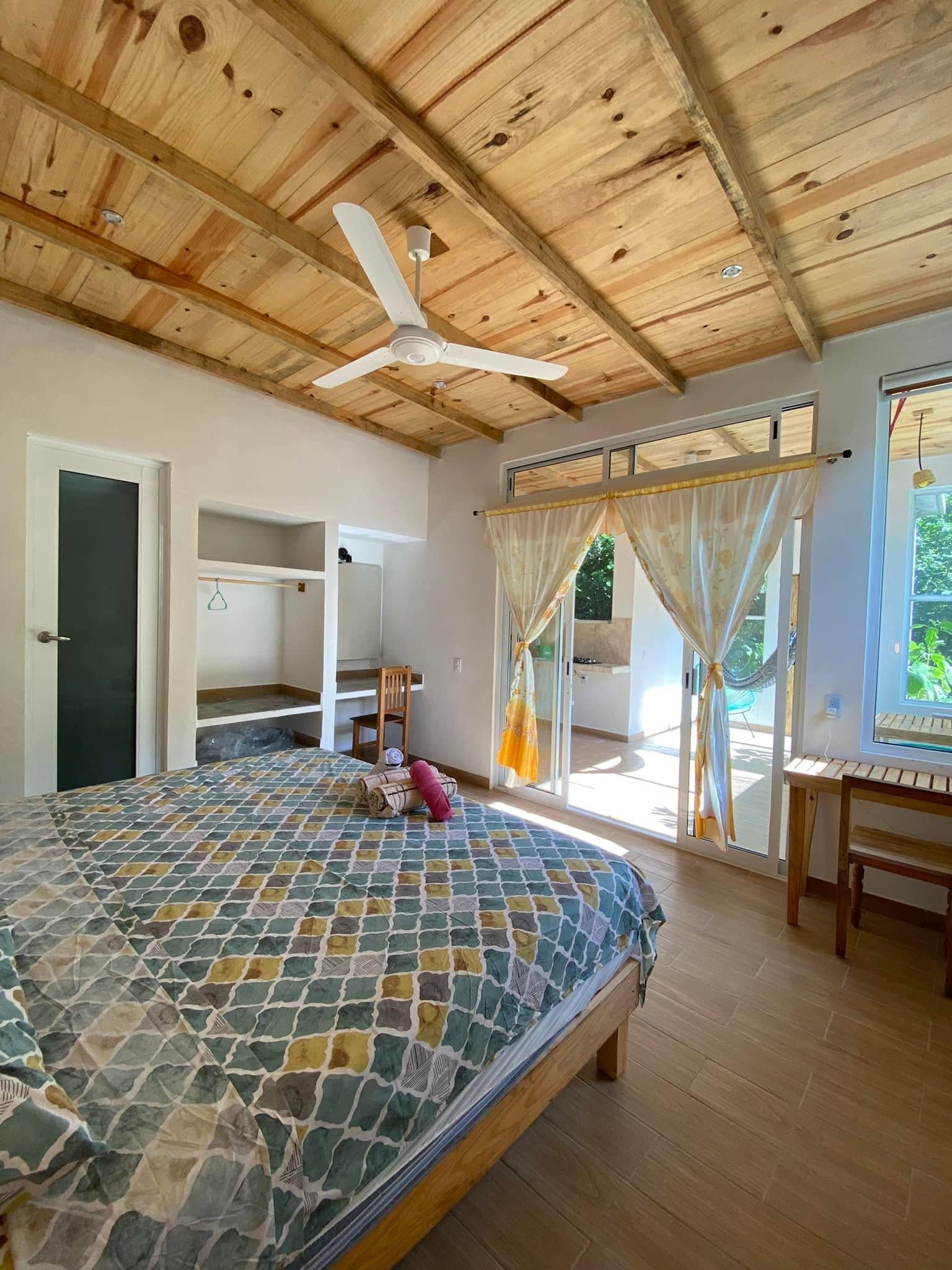 A bedroom with a bed, a chair, a ceiling fan, and a view of the outdoors.