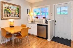A compact kitchen with a dining area, a refrigerator, a sink, and a window with a view of greenery.