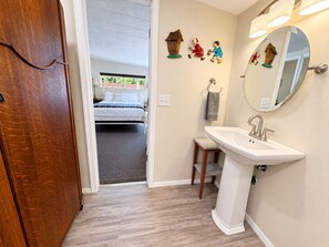 A bedroom with a bed, a wooden door, a bathroom with a sink, a mirror, and wall decorations. - Peaceful Guest Suite near Oak Creek, Trails & Cathedral Rock (Sedona)