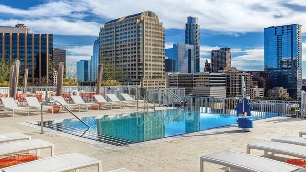 Pool på taget med liggestole og byens skyline i baggrunden.