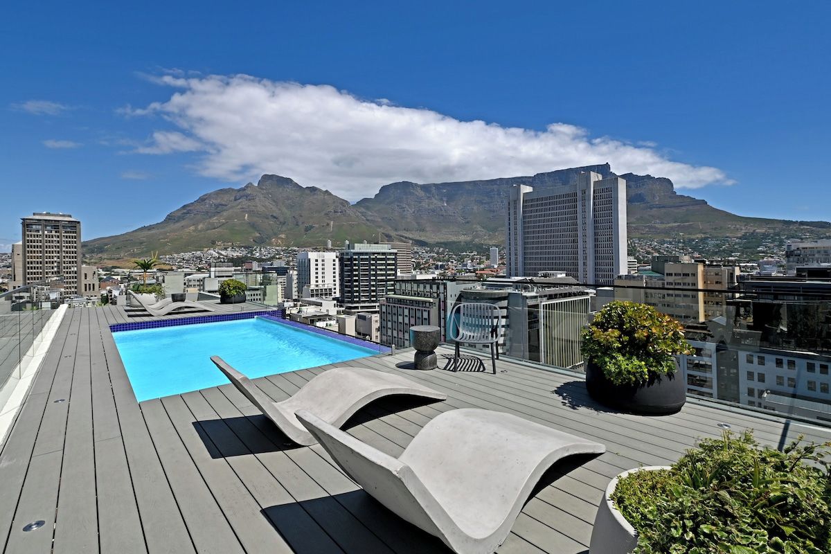 A rooftop pool with lounge chairs and a mountain view.