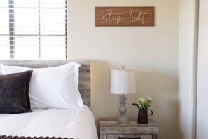 A bedroom with a bed, a nightstand with a lamp, a small plant, and a sign on the wall. - River Views + Fire Pit + Paso Robles Wine Country Views (Paso Robles)