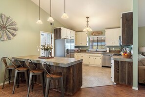 Een keuken met een centraal eiland, barstoelen, hanglampen en een decoratief wandobject.