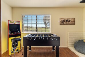 A foosball table in a room with a window, a Pac-Man arcade machine, and a framed picture on the wall. - River Views + Fire Pit + Paso Robles Wine Country Views (Paso Robles)