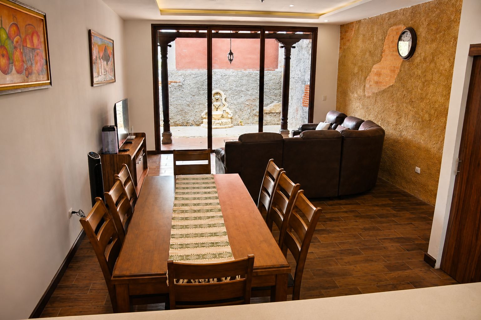 Ein Essbereich mit einem langen Holztisch und Stühlen, einer Couch und Blick durch eine Glastür auf eine Terrass.