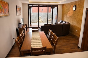 Ein Essbereich mit einem langen Holztisch und Stühlen, einer Couch und Blick durch eine Glastür auf eine Terrass.