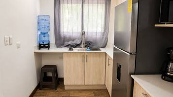 A compact kitchen with a stainless steel refrigerator, a water dispenser, and a coffee maker.