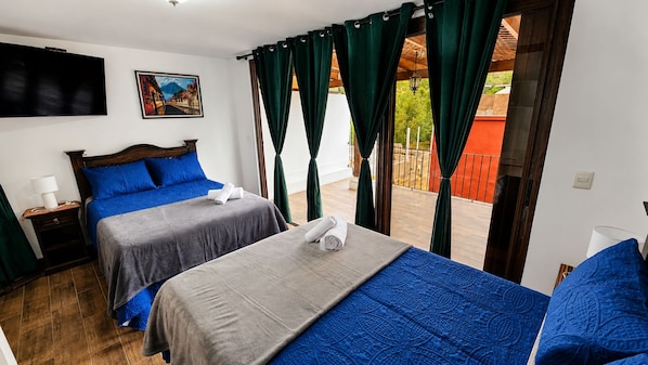 Ein Hotelzimmer mit zwei Betten, einem Fernseher und einem Balkon mit Vorhängen.