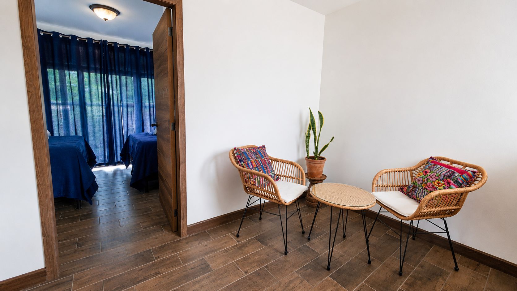 Ein Zimmer mit Holzboden, zwei Korbstühle mit Kissen, einem kleinen runden Tisch und einem Blumentopf.