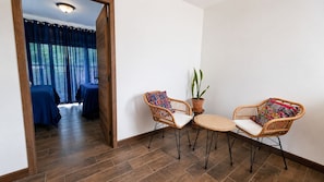 Ein Zimmer mit Holzboden, zwei Korbstühle mit Kissen, einem kleinen runden Tisch und einem Blumentopf.