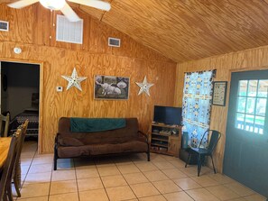Een gezellige kamer met een houten plafond, een bruine bank, een televisie en een sterrenversiering aan de muur.