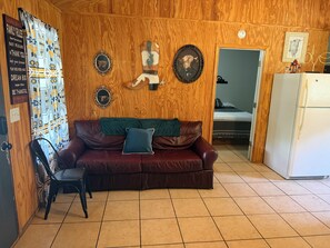 A cozy room with a brown leather couch, a green throw pillow, and a wooden wall adorned with framed pictures and a motivational poster. - 2-bedroom campground in beautiful Leakey with cozy outdoor vibes (Leakey)