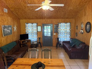 A cozy room with a wooden ceiling, a ceiling fan, a television, a dining table, two sofas, and patterned curtains. - 2-bedroom campground in beautiful Leakey with cozy outdoor vibes (Leakey)