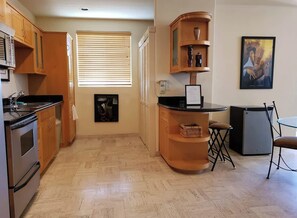 A compact kitchen with wooden cabinets, a built-in oven, a small refrigerator, and a dining area with a table and chairs. - Puerto Viejo B-1 | Waterfront 2BR on the Malecón (Puerto Peñasco)