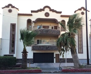 A two-story building with a balcony, a garage, and palm trees. - Puerto Viejo B-1 | Waterfront 2BR on the Malecón (Puerto Peñasco)