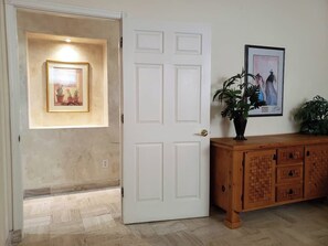 A hallway with a white door, a framed picture on the wall, a wooden cabinet, and a potted plant. - Puerto Viejo B-1 | Waterfront 2BR on the Malecón (Puerto Peñasco)