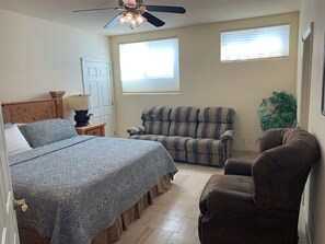Um quarto com cama, poltrona, sofá, ventilador de teto e janela.