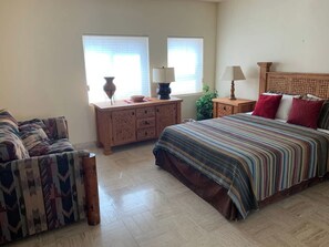 A bedroom with a bed, a sofa, a nightstand, and a dresser. - Puerto Viejo B-1 | Waterfront 2BR on the Malecón (Puerto Peñasco)