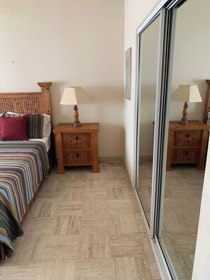 Quarto com cama, duas mesas de cabeceira com abajures, cabeceira de madeira, piso com padrão espinha de peixe e porta de vidro deslizante.