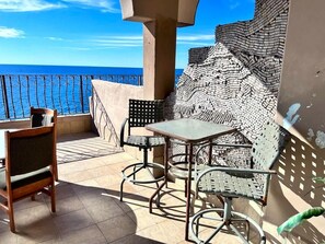 Un balcón con mesa y sillas, vista al mar y una pared con diseño.