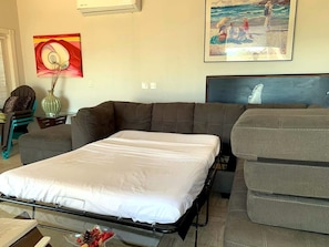A room with a bed, a sofa, and a chair. There are paintings on the wall. - Puerto Viejo C-2 | Waterfront 3BR on the Malecón (Puerto Peñasco)