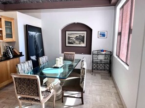 Un comedor con mesa de vidrio, sillas acolchadas y un cuadro enmarcado en la pared.